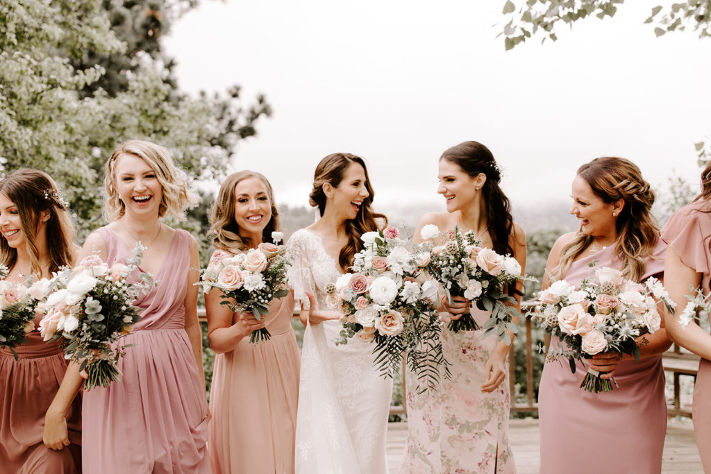 Bride laughing with bridesmaids in blush dresses.