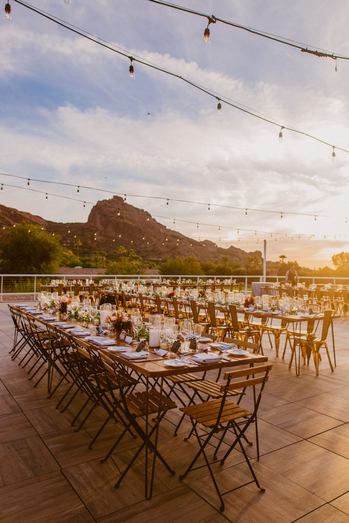 Paradise Valley Wedding - patio outdoor reception with unique long tables at this modern wedding and fall Arizona wedding. The greenery with warm colors wedding color palette was seen in the wedding flower arrangements, centerpieces, and arch flowers. Greenery bouquets, greenery boutonnières, and greenery with floral arrangements were also included. The fall wedding flower colors included a range of red, pink, orange, and peach, perfect to match the fall desert wedding sunset. Photos by Olivia Markle. #fallwedding #weddingflowers #weddings #weddingreception