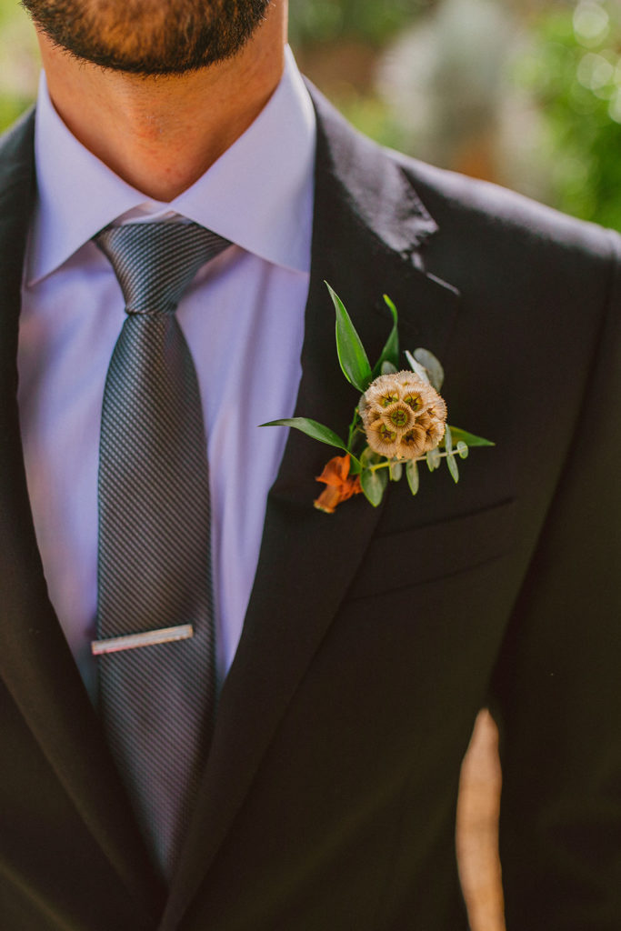 Paradise Valley Wedding - Unique greenery scabiosa pod boutonniere at this modern wedding and fall Arizona wedding. The greenery with warm colors wedding color palette was seen in the wedding flower arrangements, centerpieces, and arch flowers. Greenery bouquets, greenery boutonnières, and greenery with floral arrangements were also included. The fall wedding flower colors included a range of red, pink, orange, and peach, perfect to match the fall desert wedding sunset. Photos by Olivia Markle. #fallwedding #weddingboutonniere #weddingflowers #weddings
