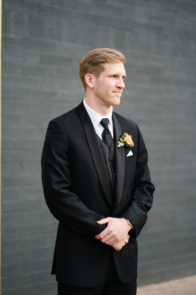 Arizona Modern Spring Wedding - the perfect groom in black suit at an elegant and modern urban wedding at The Venue on Washington in Phoenix. The gold wedding flowers with peach and white in the wedding color palette was seen in the wedding flower arrangements, bridal bouquet, bridesmaid bouquets, boutonniere, and bud vases of gold roses. The spring wedding flowers included roses, ranunculus, blue thistle, and greenery. Photos by Emily B. #wedding #springwedding #weddingflowers