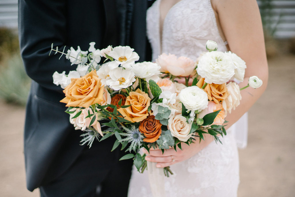 Arizona Modern Spring Wedding - the perfect bridal bouquet at an elegant and modern urban wedding at The Venue on Washington in Phoenix. The gold wedding flowers with peach and white in the wedding color palette was seen in the wedding flower arrangements, bridal bouquet, bridesmaid bouquets, boutonniere, and bud vases of gold roses. The spring wedding flowers included roses, ranunculus, blue thistle, and greenery. Photos by Emily B. #wedding #springwedding #weddingflowers
