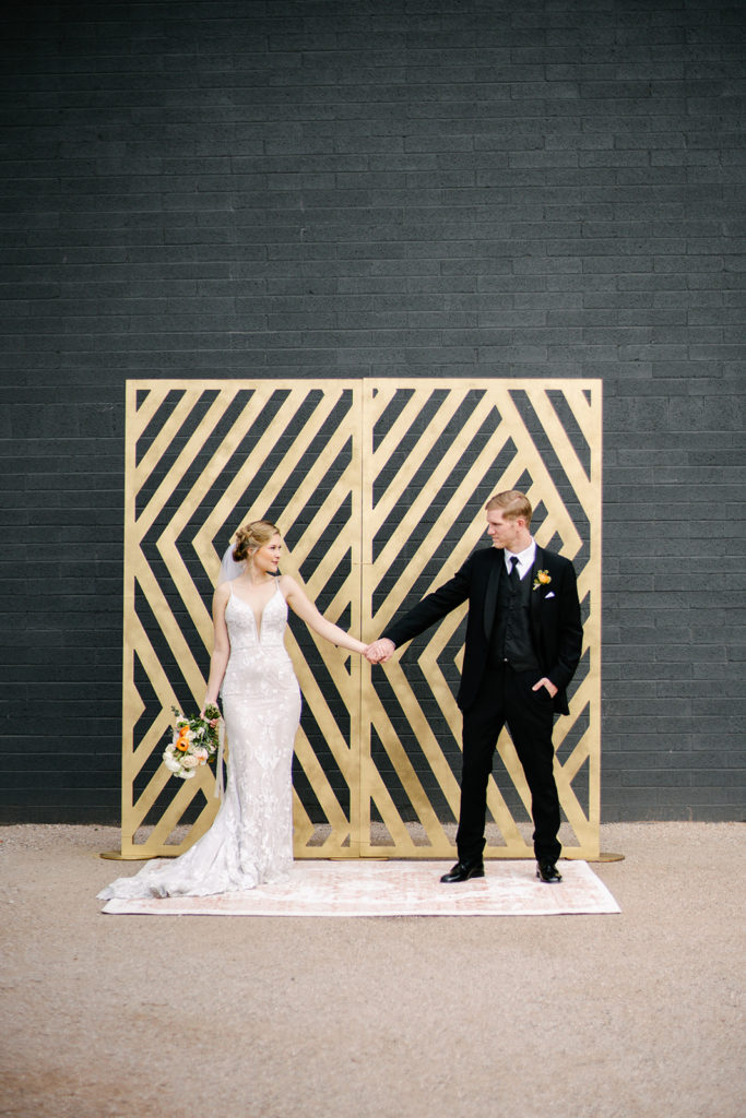 Arizona Modern Spring Wedding - the perfect gold geometric ceremony backdrop for an elegant and modern urban wedding at The Venue on Washington in Phoenix. The gold wedding flowers with peach and white in the wedding color palette was seen in the wedding flower arrangements, bridal bouquet, bridesmaid bouquets, boutonniere, and bud vases of gold roses. The spring wedding flowers included roses, ranunculus, blue thistle, and greenery. Photos by Emily B. #wedding #springwedding #weddingflowers