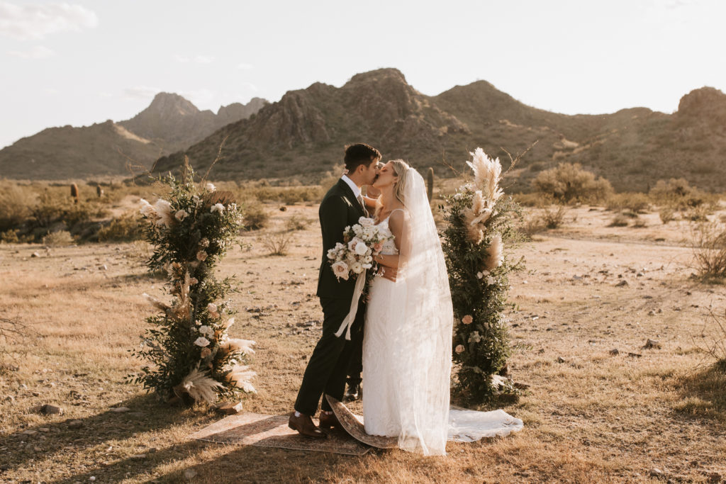 Boho Arizona Desert Ceremony - the perfect intimate desert outdoor wedding ceremony. The blush and white wedding flowers with dusty pink wedding color palette was seen in the wedding flower arrangements, ceremony decor, wedding bouquets, wedding ceremony backdrop outdoor, and wedding flowers. The boho wedding flowers included pampas grass, roses and greenery. Wedding ceremony altar of pampas grass, roses and greenery. Photos by Madi Robison. #weddingbouquets #desertwedding #weddingflowers #weddings