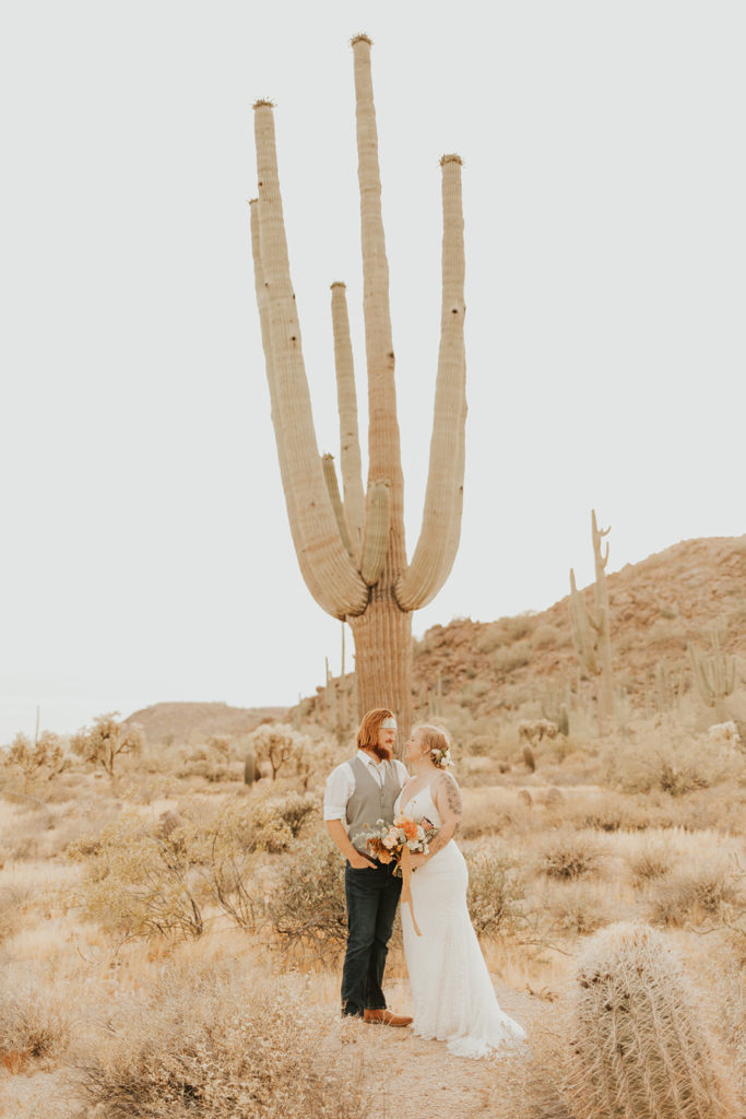 Bride and groom posing in front of saguaro cactus.