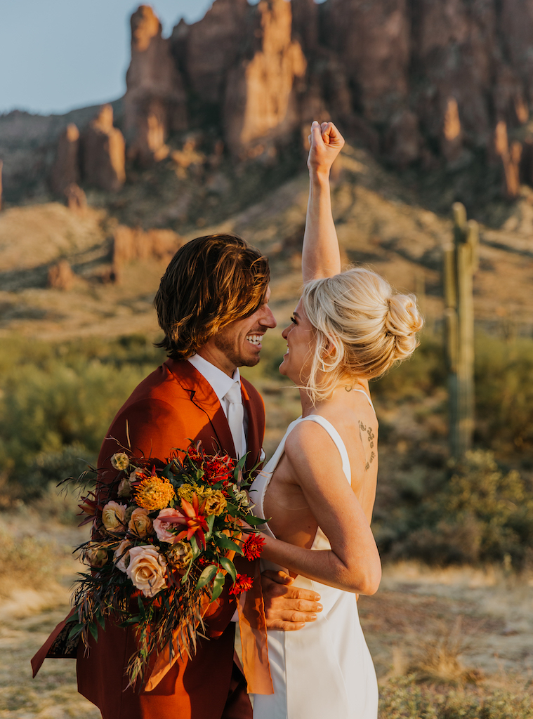 Groom with bride smiling at each other in desert.