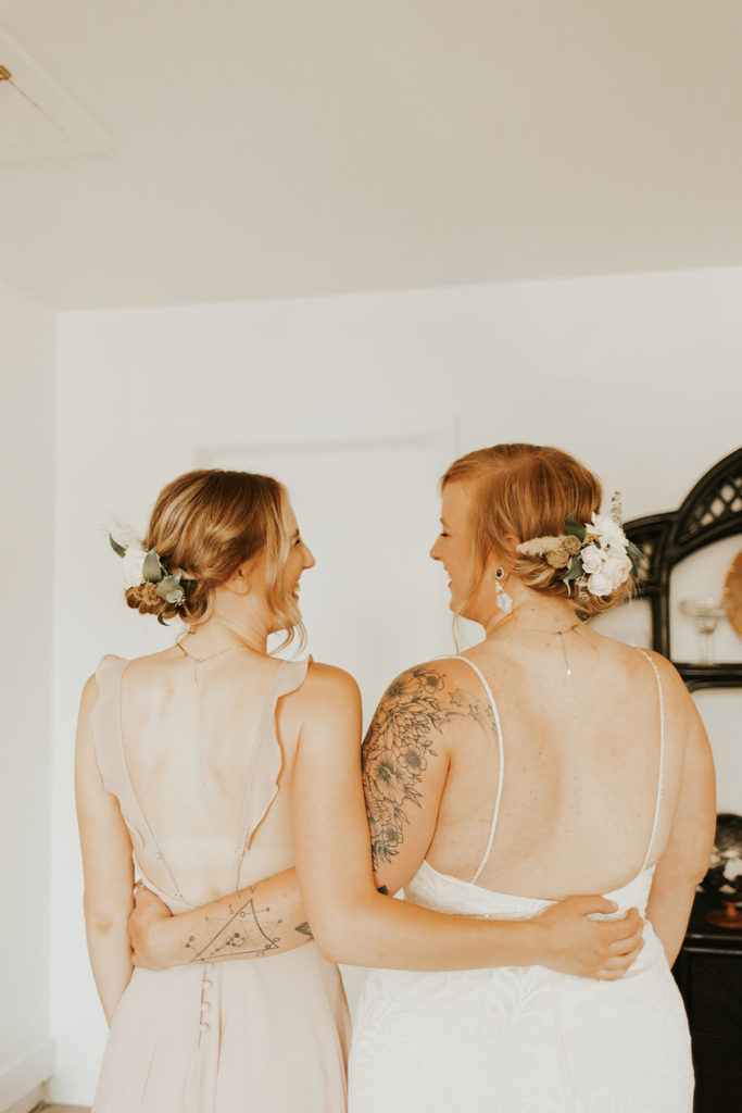 Bride and bridesmaid with arms around each other.