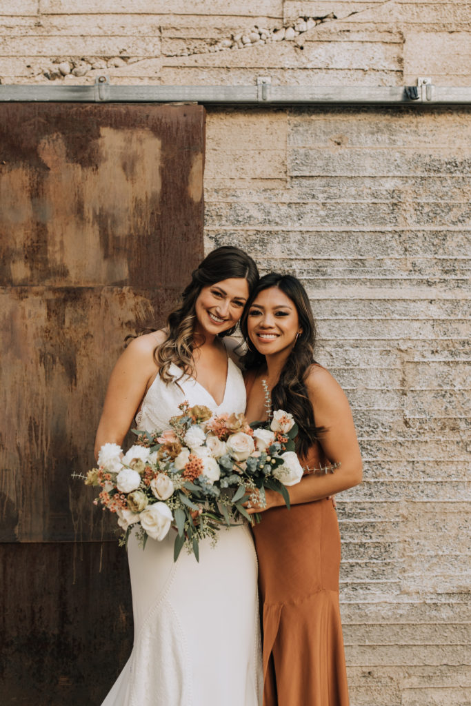 Bride with bouquet and bridesmaid in burnt orange dress.
