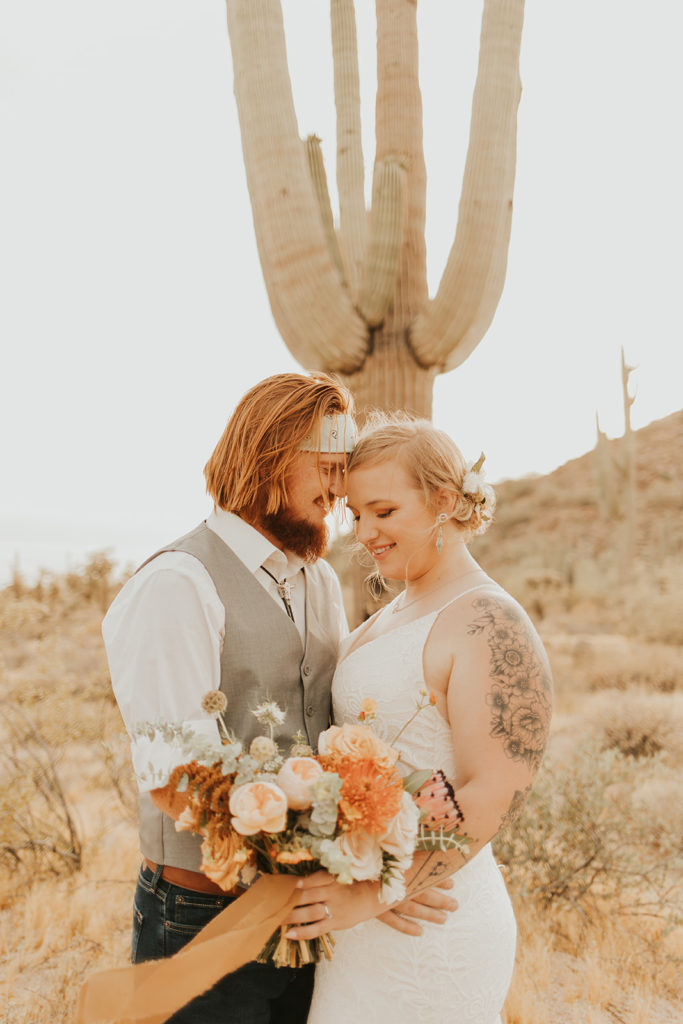 Groom and bride holding bouquet in desert.