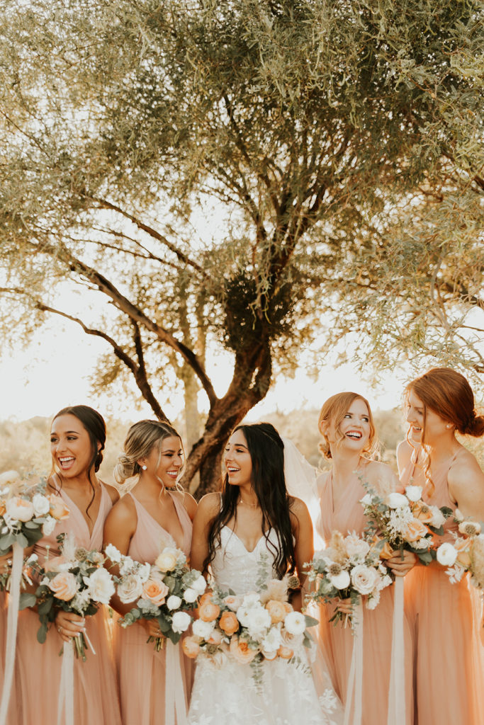 Bride with bridesmaids holding bouquets and laughing