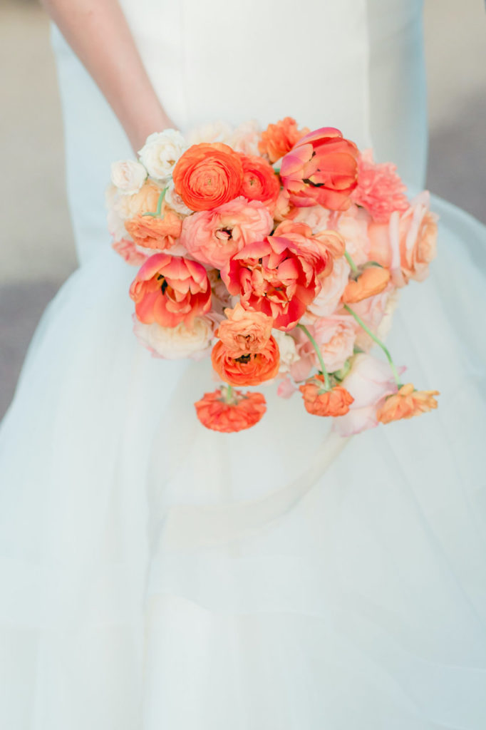 Bride holding peach colored flowers bouquet.