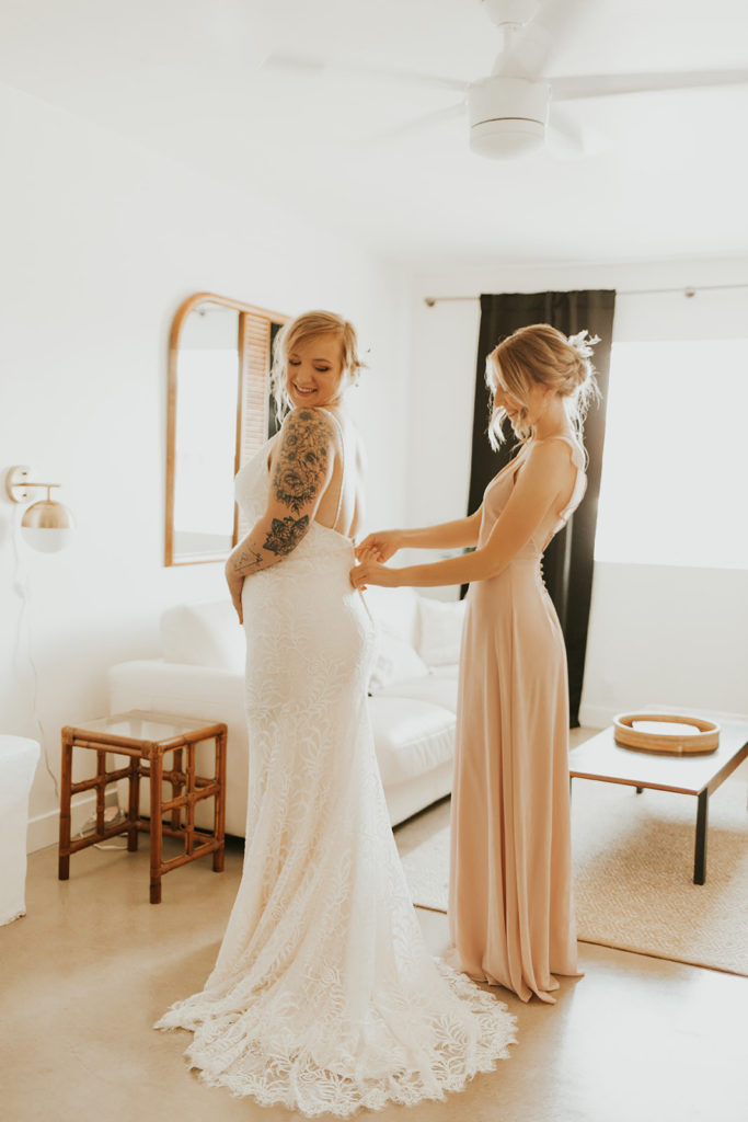 Bridesmaid zipping up bride's gown.