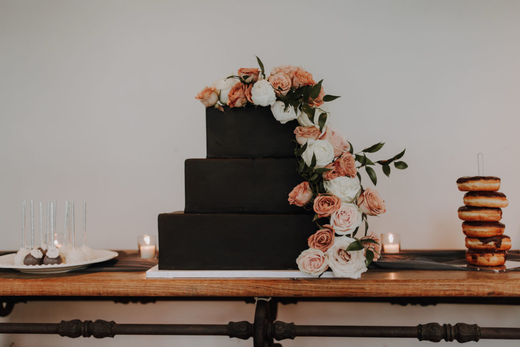 Black tiered wedding cake with cascading flowers.