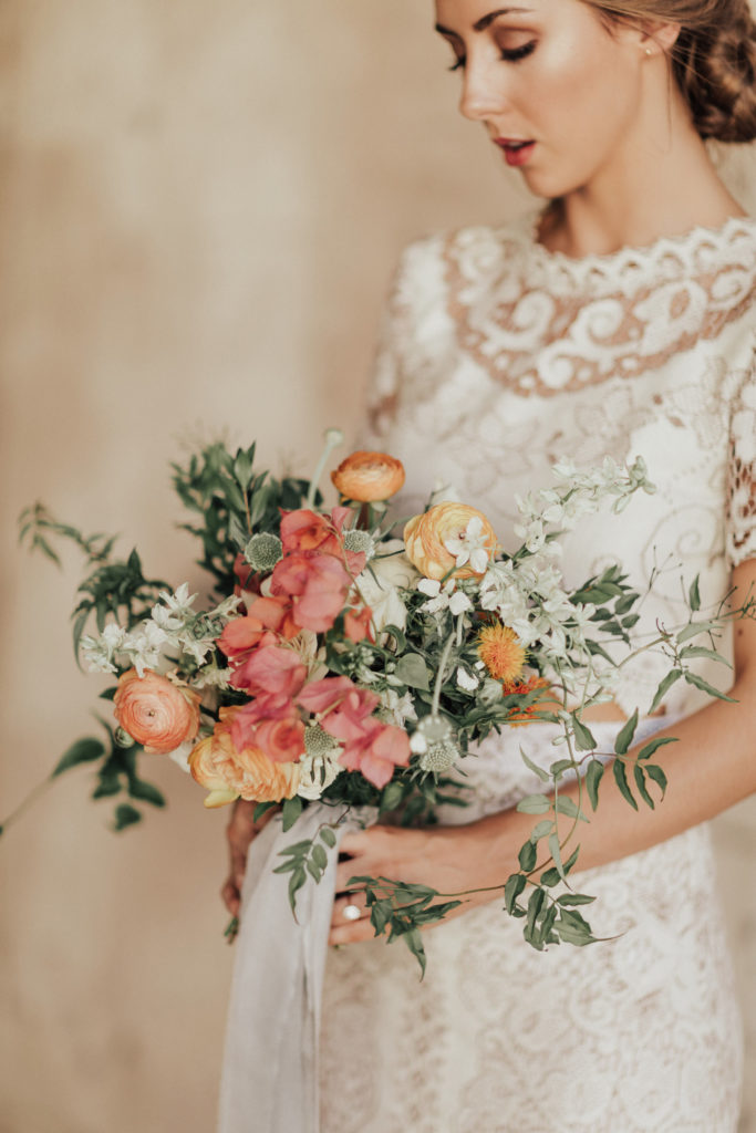 Bride holding bouquet of pink and orange flowers.