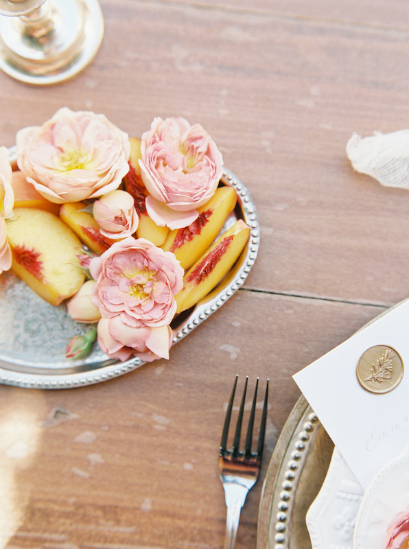 Peaches on a silver platter with peaches and pink flowers.