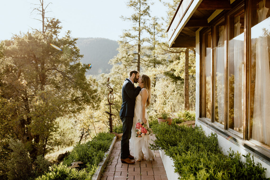 Bride and groom kissing outside house in forest.