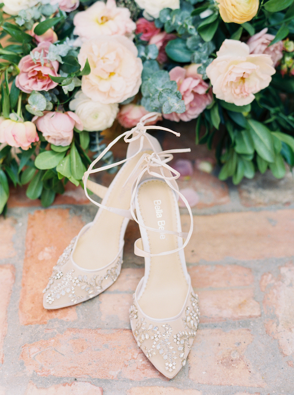 White detailed wedding shoes next to flowers.