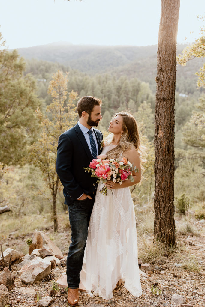 Bride holding bouquet looking at groom in mountains.
