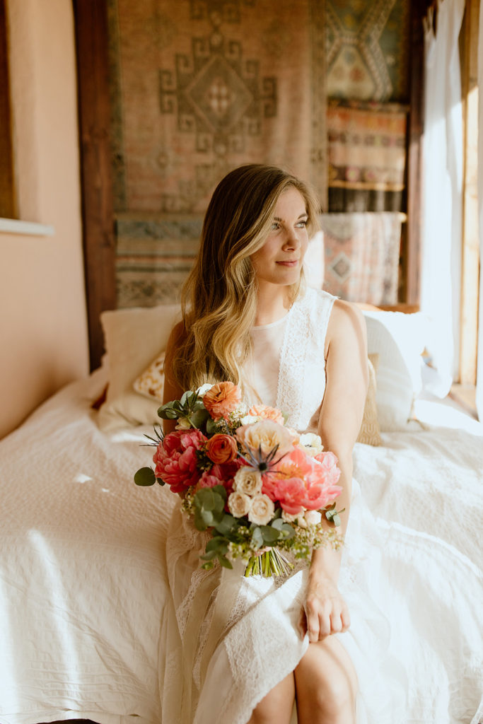 Bride sitting on bed holding bouquet.