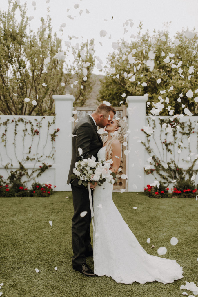 Bride and groom kissing in white flower petals falling.