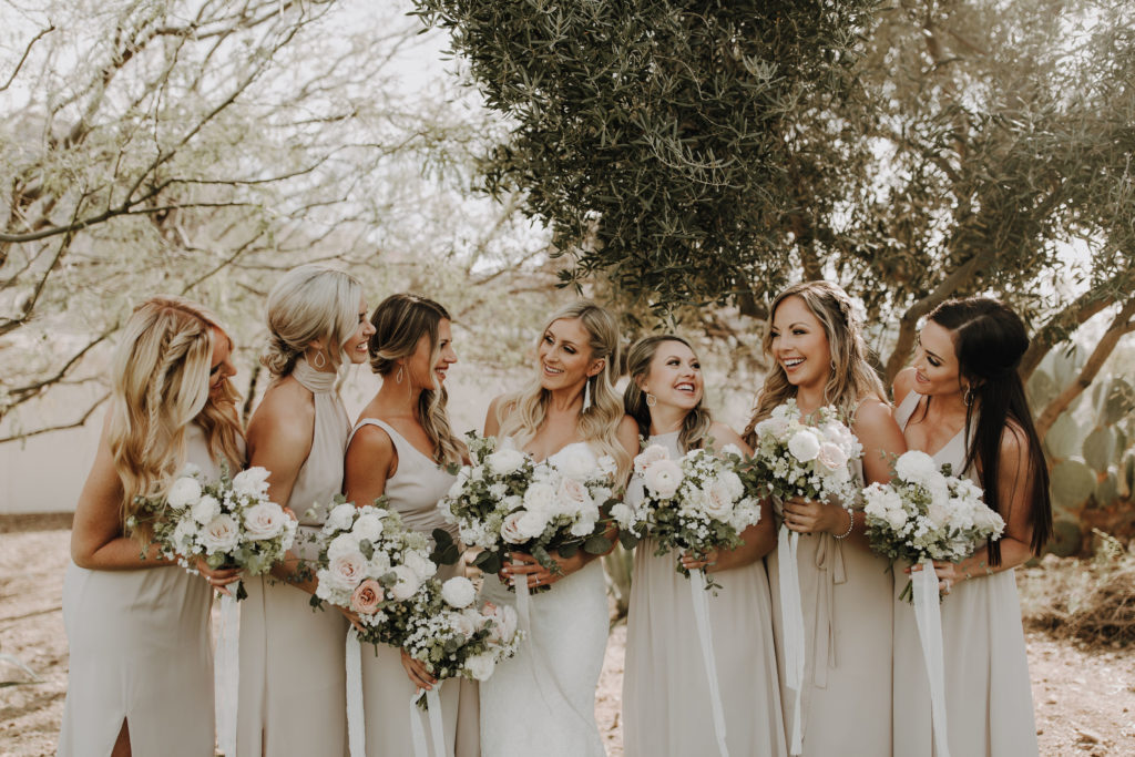 Bride with bridesmaids in a line smiling, holding bouquets.