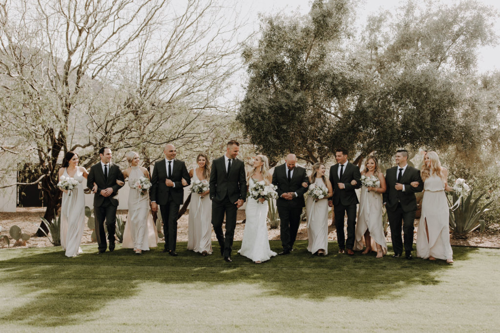 Wedding party walking forwards with arms linked.
