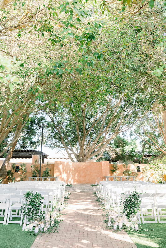 Outdoor wedding ceremony with greenery and pillar candles on last aisle's chair at Royal Palms resort.