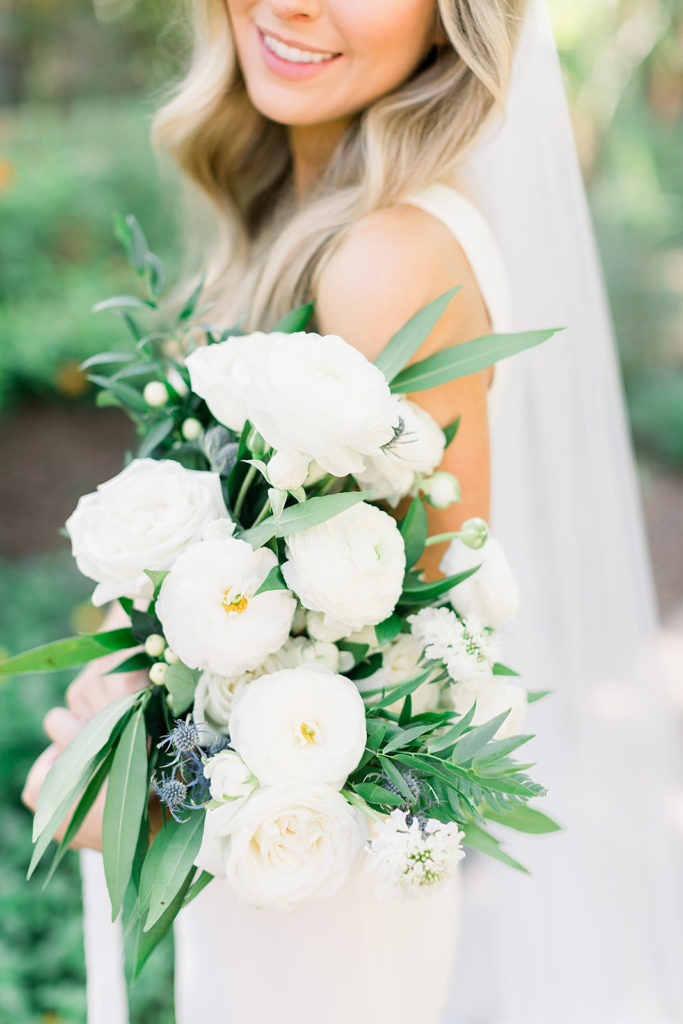 Bride holding white flowers bridal bouquet, smiling down.