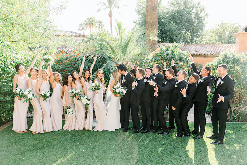 Wedding party of bridesmaids and groomsmen celebrating with bride and groom kissing in the center of lined up bridal party.