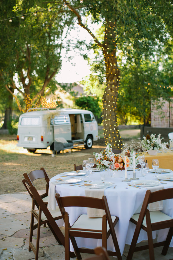 Outdoor wedding reception with round tables at Phoenix estate wedding venue and cream colored photo bus in background.