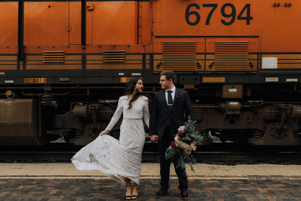 Couple holding hands in front of train.