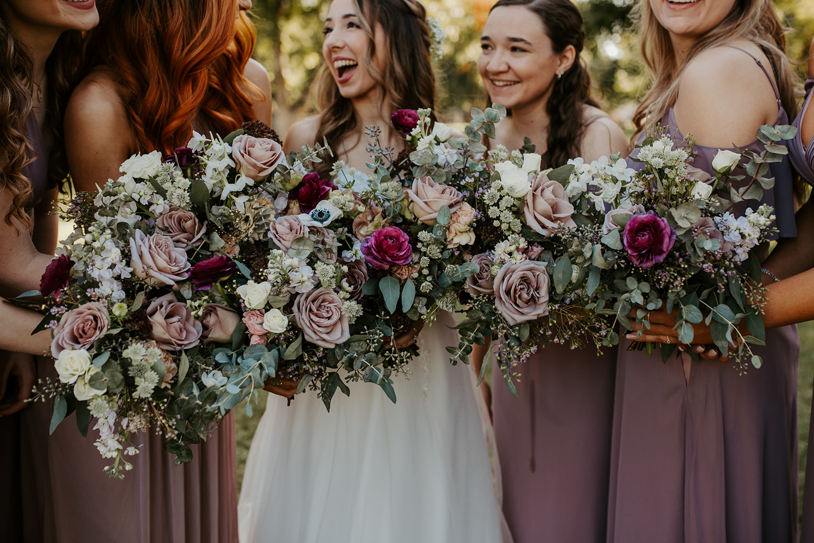 Bride and bridesmaids holding bouquets with purple flowers and dresses.