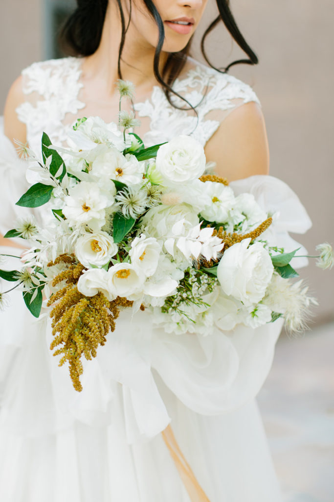 Bride holding fall wedding bouquet of white flowers with orange floral details.