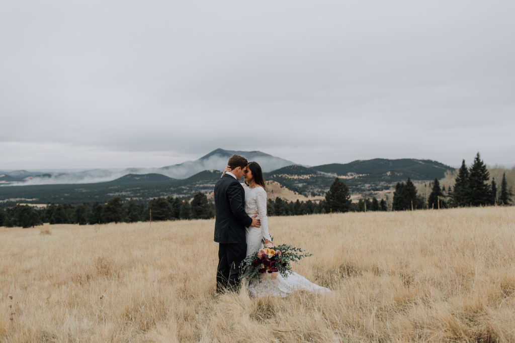 Couple in Flagstaff field embracing with a mountain in the distance.