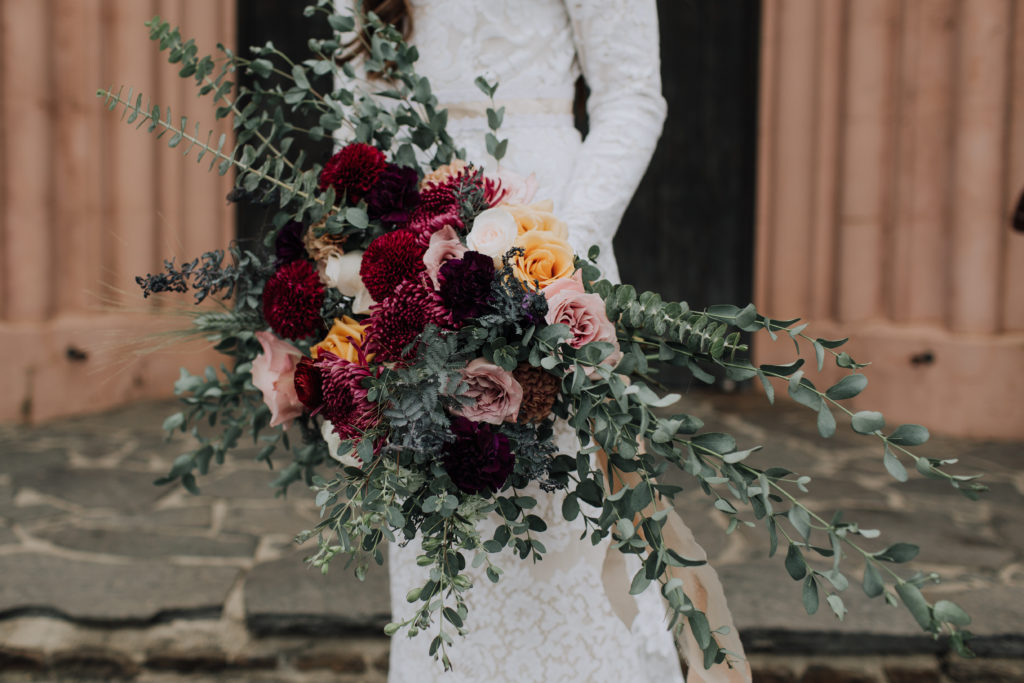 Bridal bouquet of maroon, yellow and blush flowers with spiral eucalyptus and other greenery.