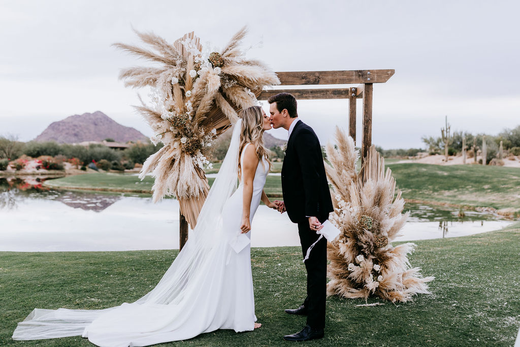 Outdoor wedding ceremony with boho wedding floral installation on arch.