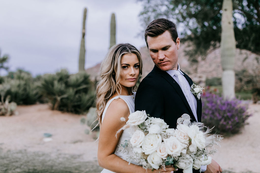 Bride and groom in desert setting at Troon Country Club, bride holding white and blush rose bouquet.