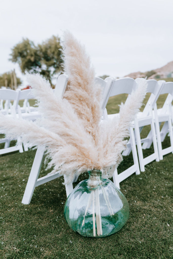 Dried pampas in glass round vase at back of Arizona wedding ceremony aisle.