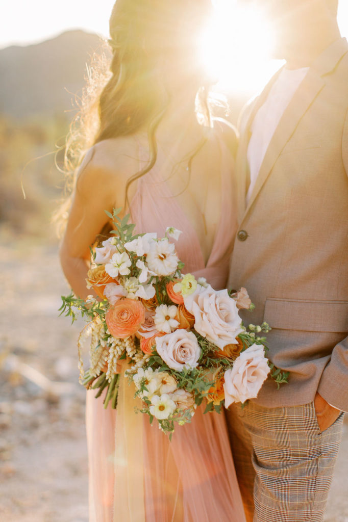 Sun rays shining between wife and husband standing next to each other, looking at each other. She is holding a flower bouquet.