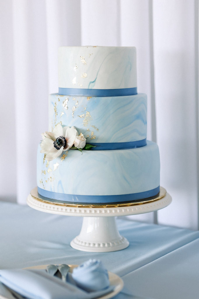 Three tiered wedding cake with white and blue marble design with gold and an anemone flower.