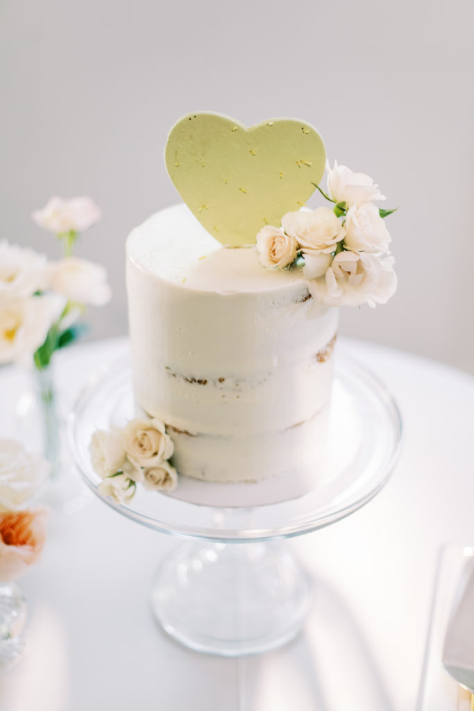 White three tiered wedding cake with green heart cactus topper and flowers.