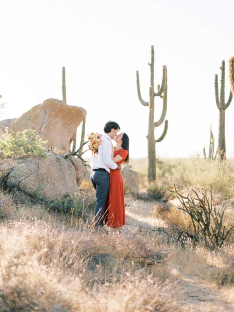 Couple standing in desert embracing, girl holding bouquet.
