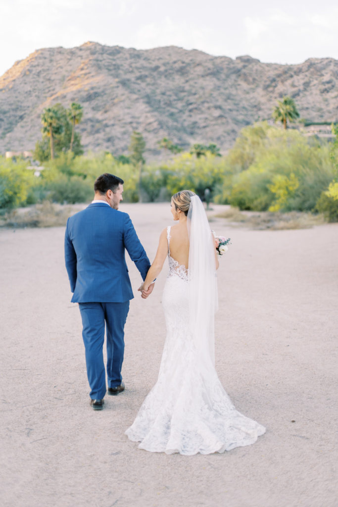 Bride and groom holding hands walking away in desert.