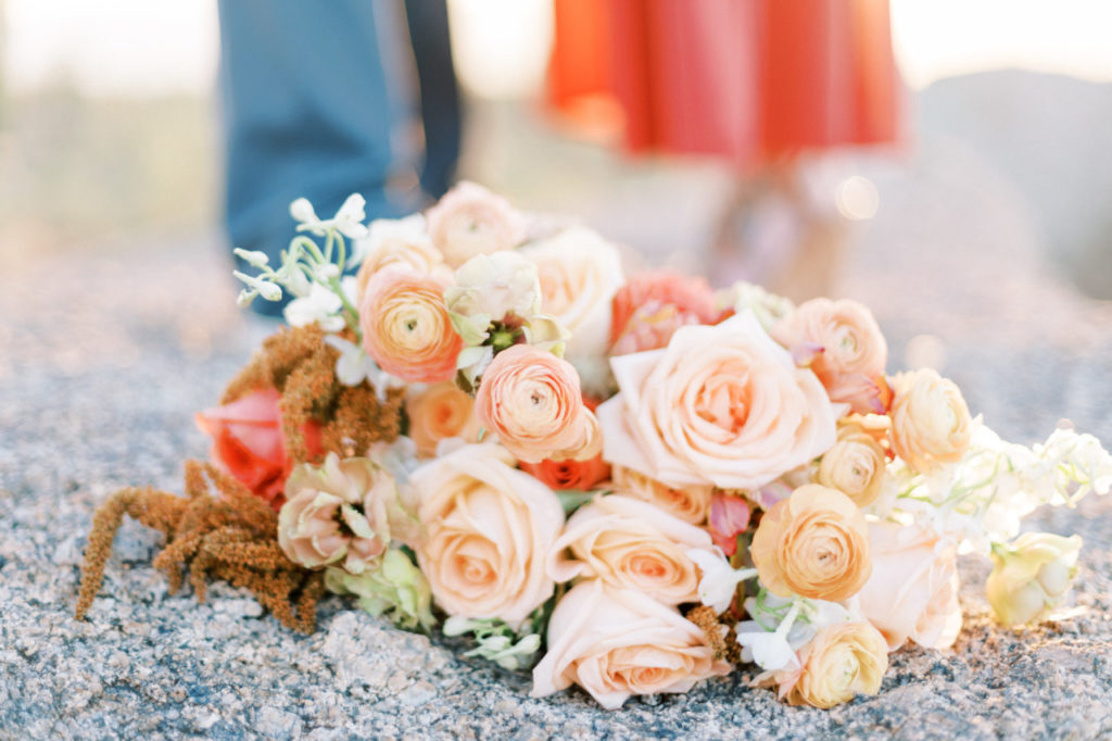 Bridal bouquet of pink, peach, coral colors, resting on boulder in the desert.
