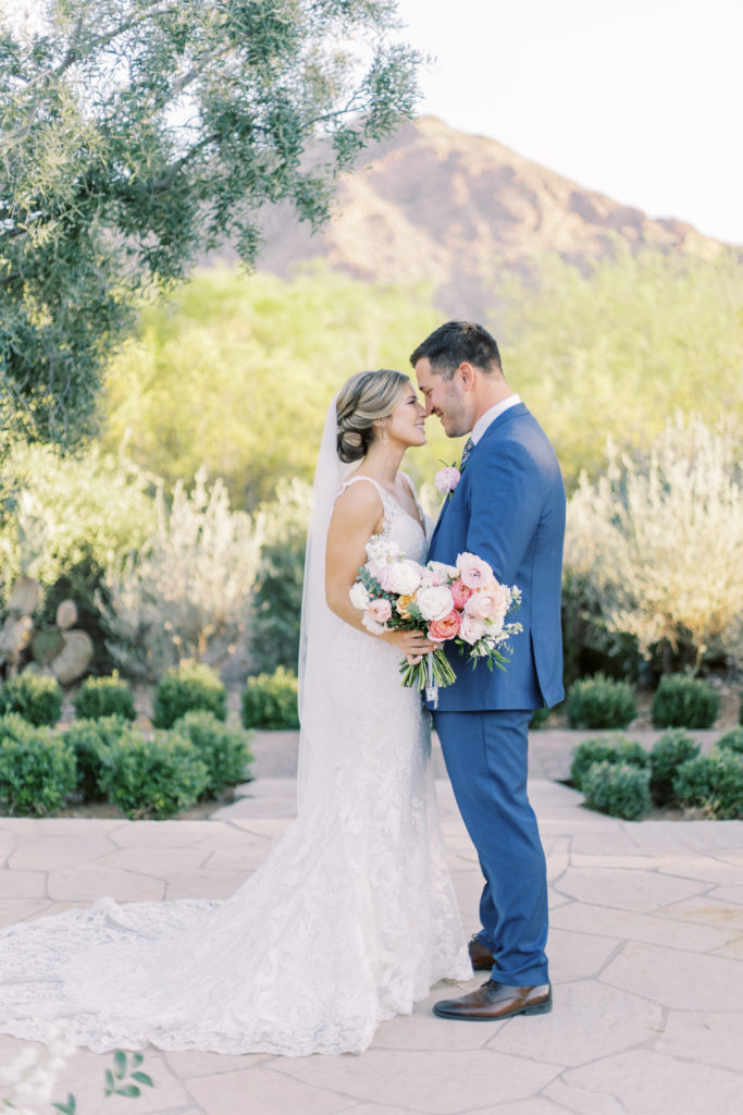 Bride and groom nose to nose, embracing in front of desert mountain landscape.