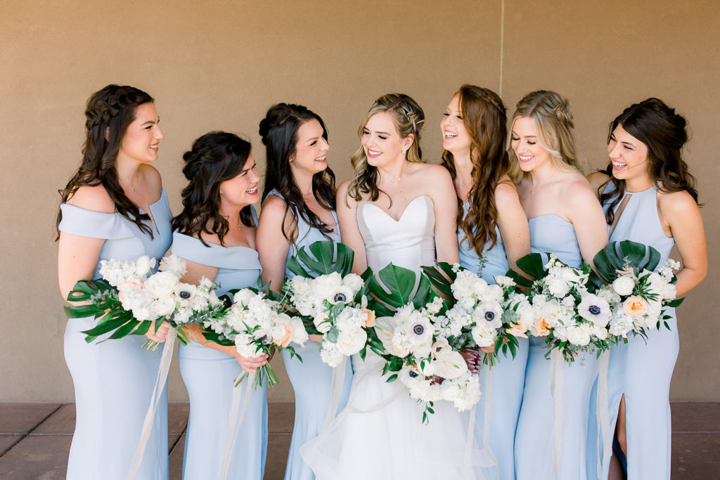Bride with bridesmaids in light blue dresses, holding bouquets, looking at one another.