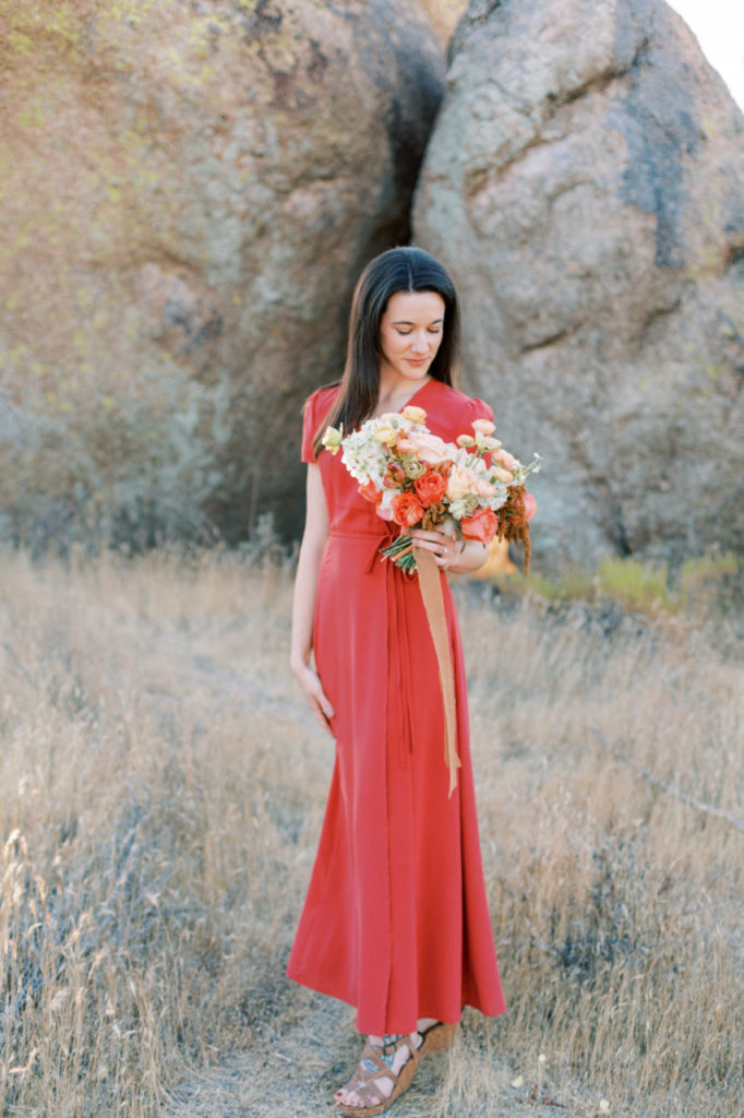 Woman in coral dress looking down at bouquet she is holding.