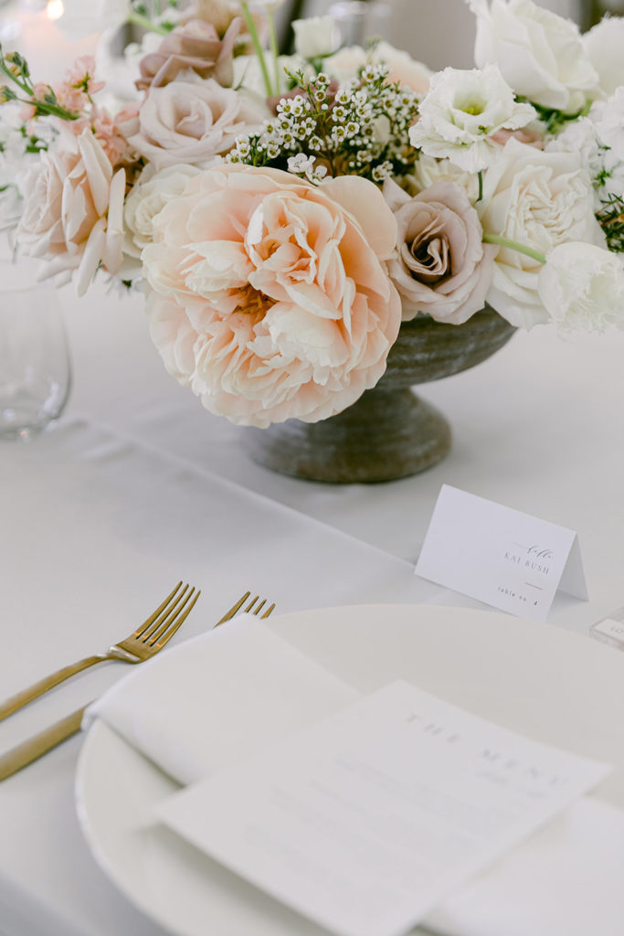 Wedding reception place setting with floral centerpiece, gold flatware.