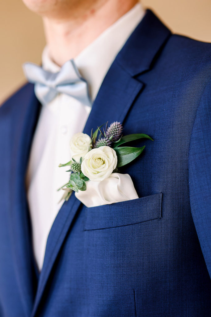 Groom boutonniere of white flowers and blue thistle and greenery.