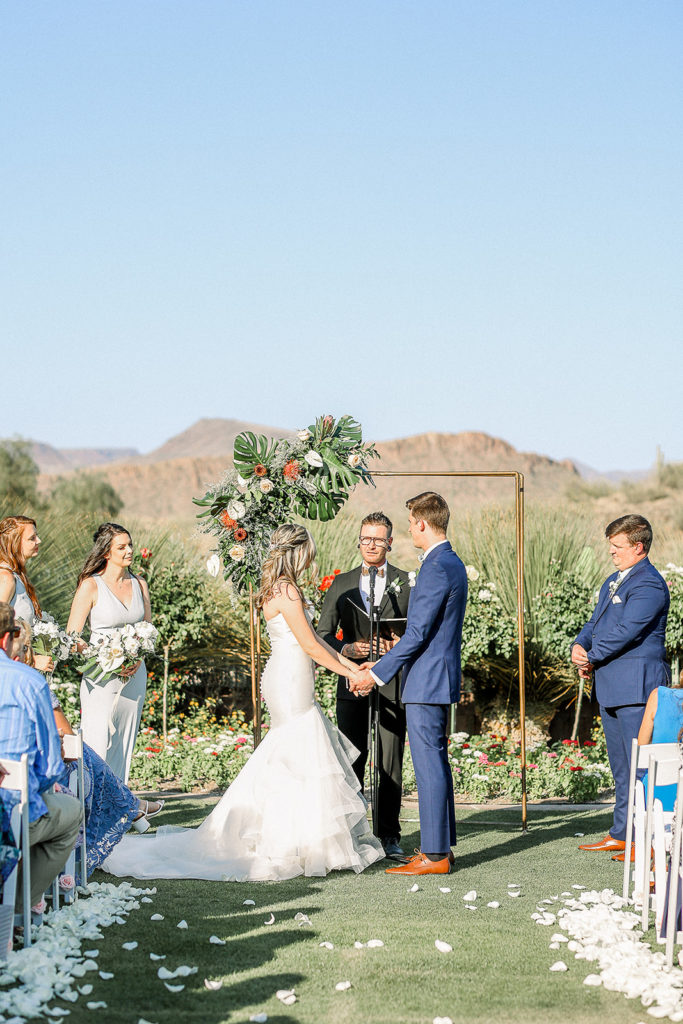 Bride and groom holding hands in front of officiant and wedding arch at Anthem Arizona wedding ceremony.
