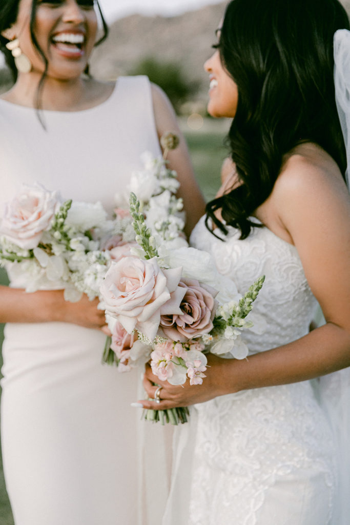 Bride and bridesmaid talking, holding bouquets.